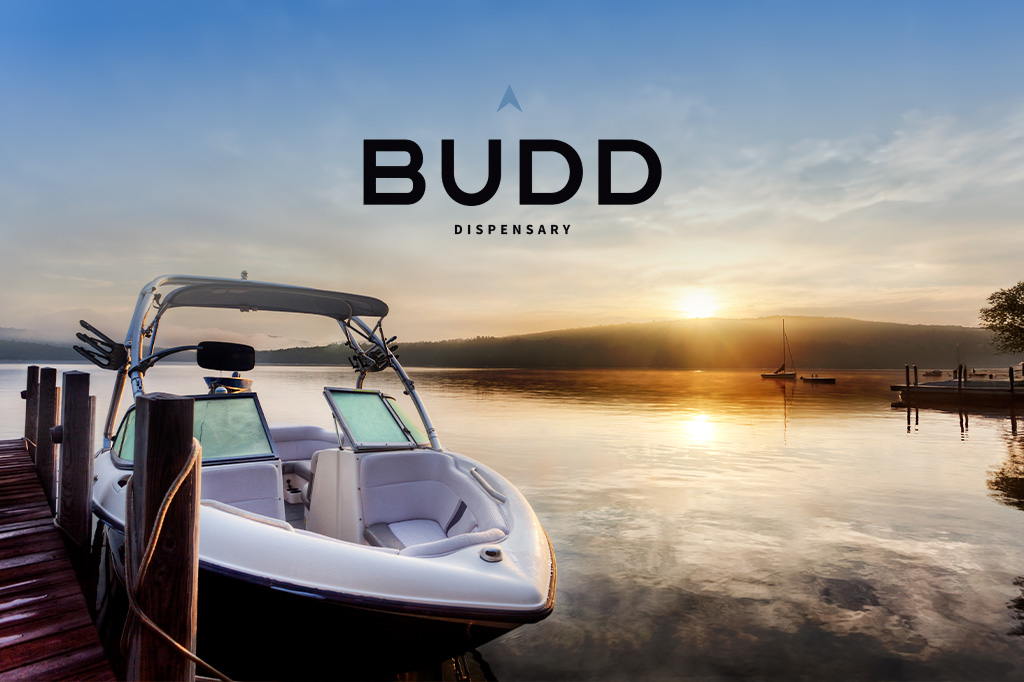 Peaceful sunrise over a glassy lake with a docked boat in the foreground and BUDD Dispensary logo above.
