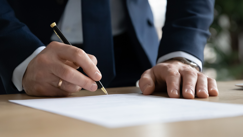 lawyer in a suit signing a paper on a desk with a pen