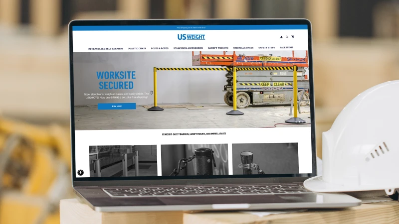 Laptop displaying the US Weight website homepage featuring worksite safety products, with a construction hard hat beside the computer to represent industrial and workplace safety solutions.