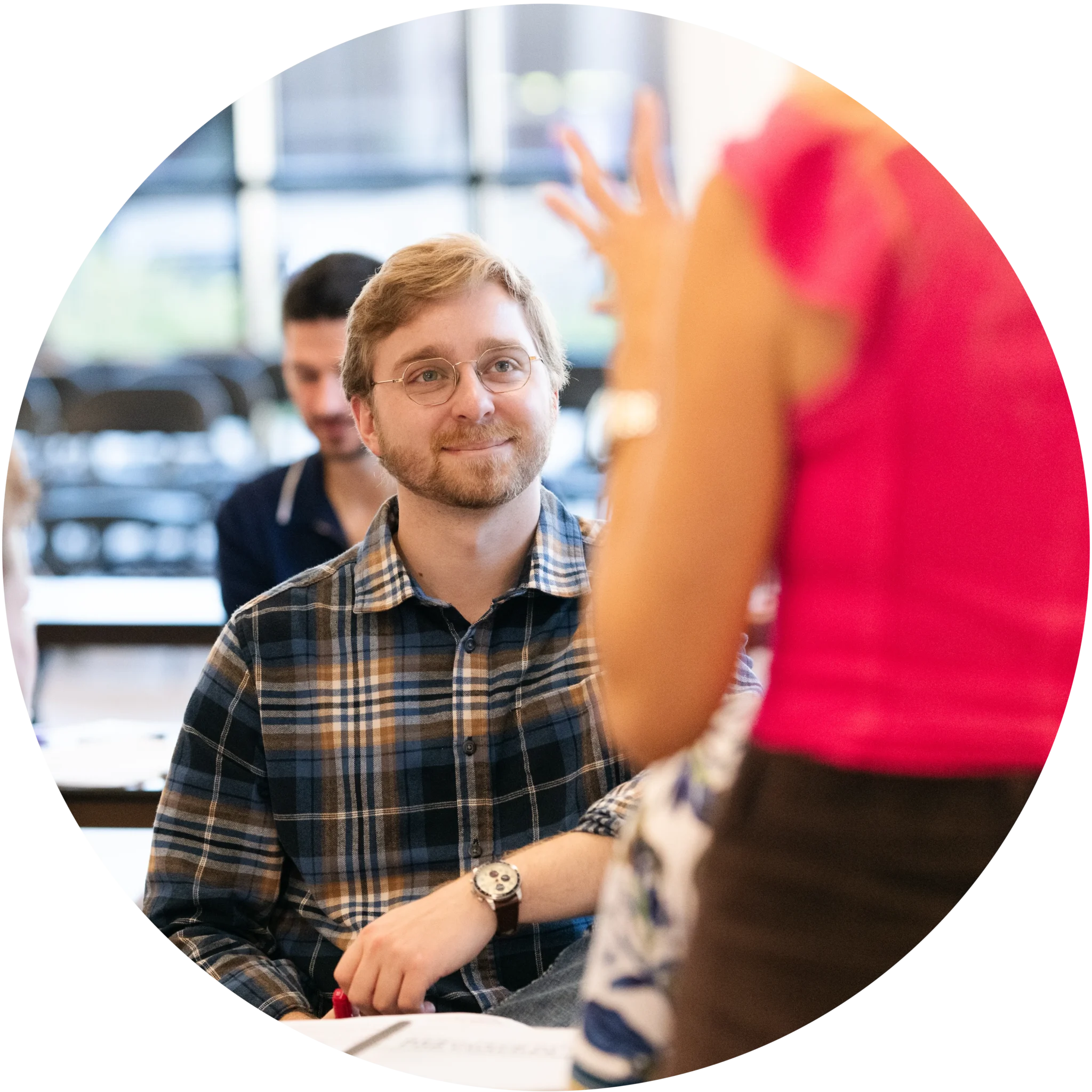 A young man looks up, smiling and listening, as someone discussing marketing strategy.