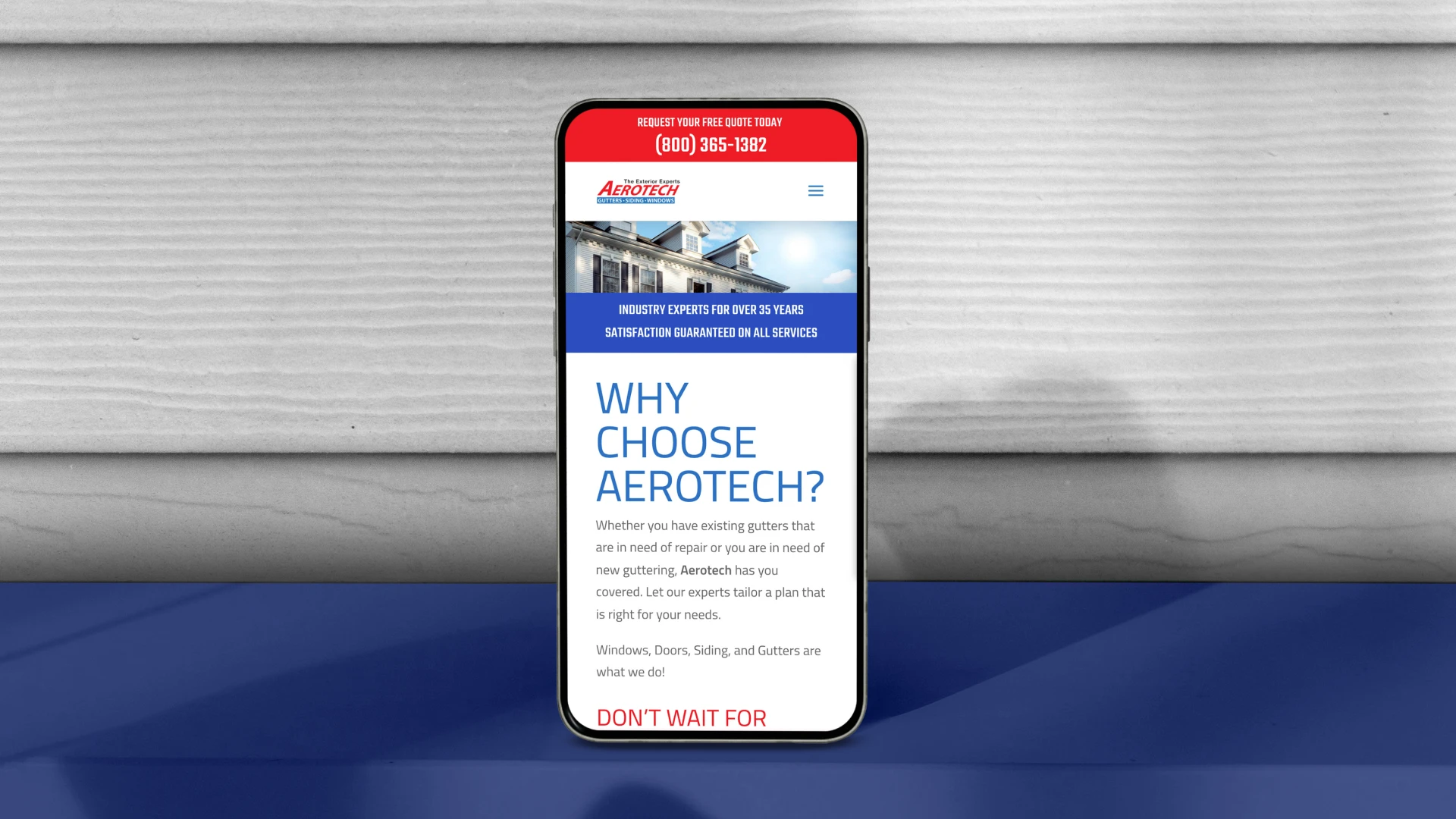 Smartphone displaying Aerotech's website with a focus on gutter services, highlighting a red contact number. The background shows wood paneling.