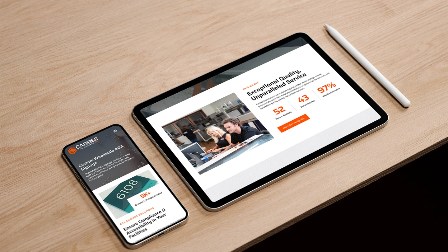 A tablet and smartphone on a wooden desk display business websites. The tablet shows a service page with happy coworkers. A stylus lies beside it.
