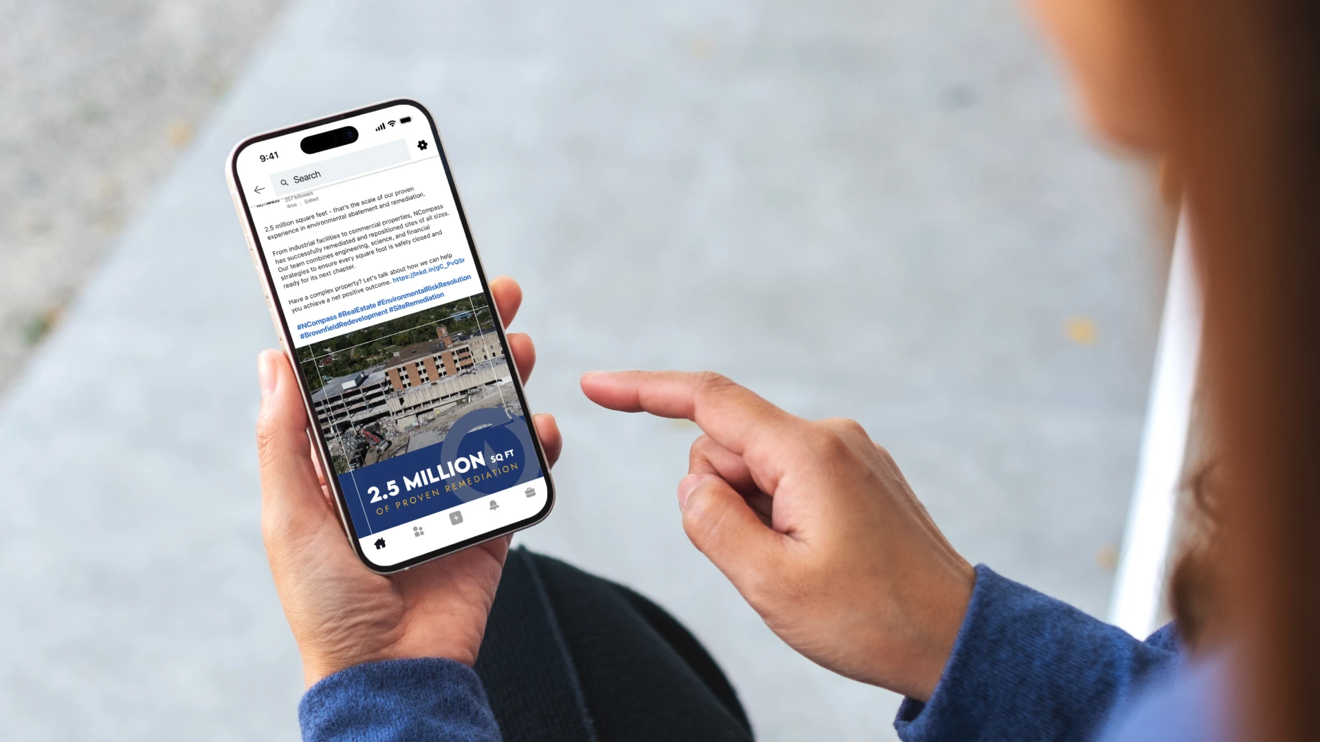 A person is holding a smartphone, displaying a newsletter with text and an image of buildings. The screen highlights "2.5 MILLION SQ FT" in bold.