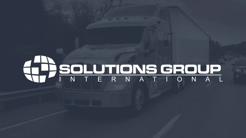 A semi-truck drives down a highway in a tinted image. Overlaid text reads “Solutions Group International” with a globe logo, conveying professionalism.