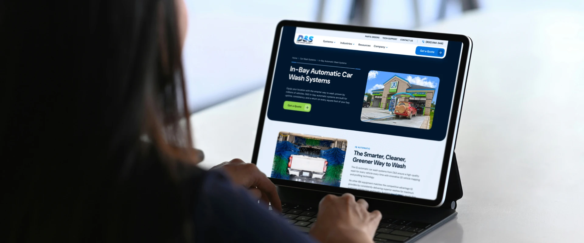 Person typing on a tablet showing a blue car wash website about In-Bay Automatic Car Wash Systems.