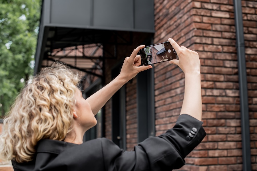 Person with blonde hair wearing a dark suit taking video of a building