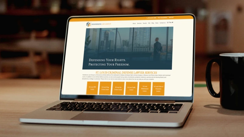 A laptop displays a law firm's website highlighting criminal defense services. The webpage features the St. Louis skyline and a serious, professional tone.