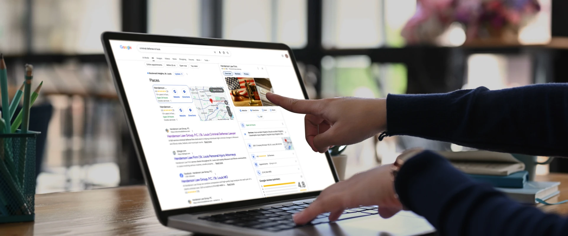 Person points at a laptop screen displaying Google search results for "criminal defense st louis," which includes a map and listings.