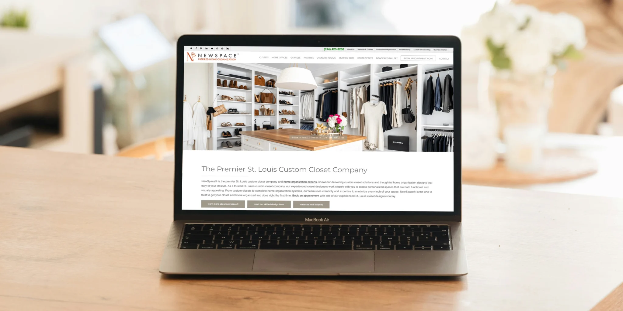 Laptop on a wooden table showing a boutique closet website with white shelving, shoes, bags and clothes inside a bright room