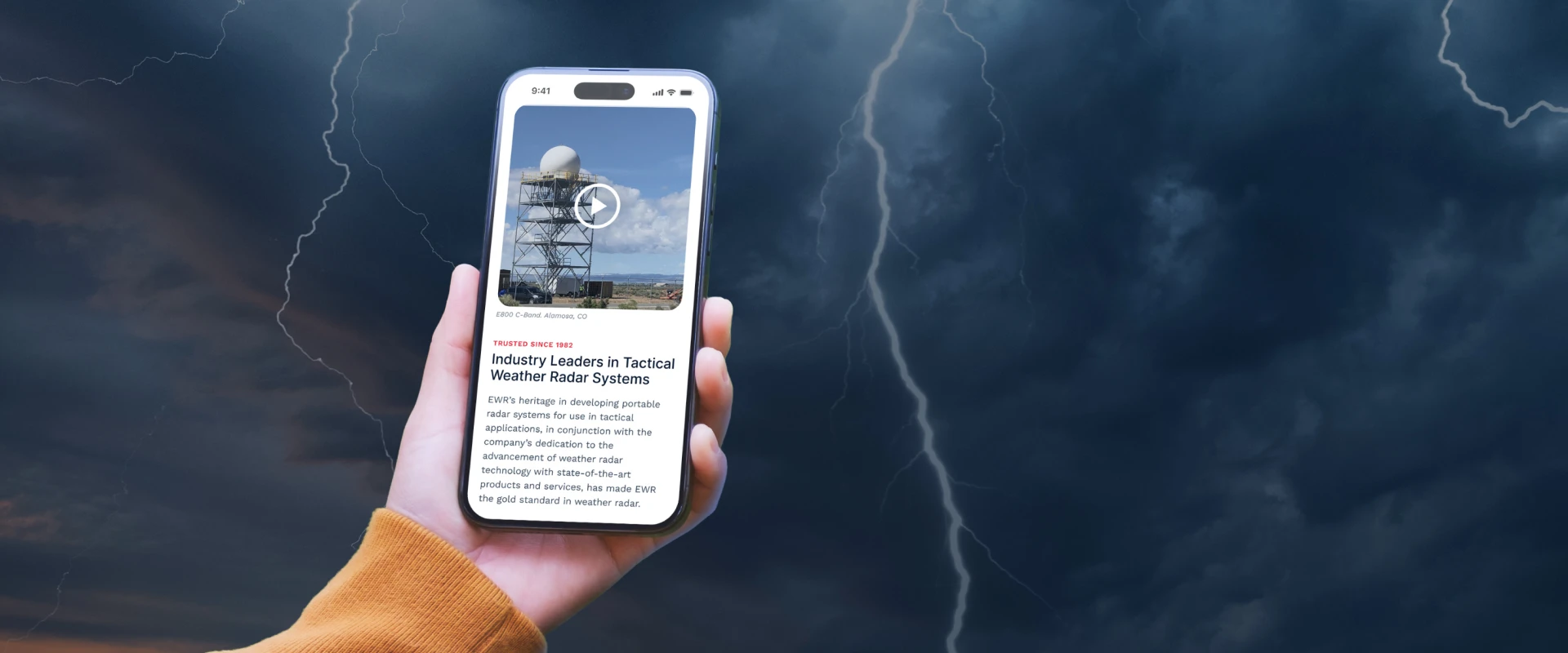 EWR Radar Systems mobile website displayed on a smartphone against a stormy sky, featuring tactical weather radar technology and a radar tower.